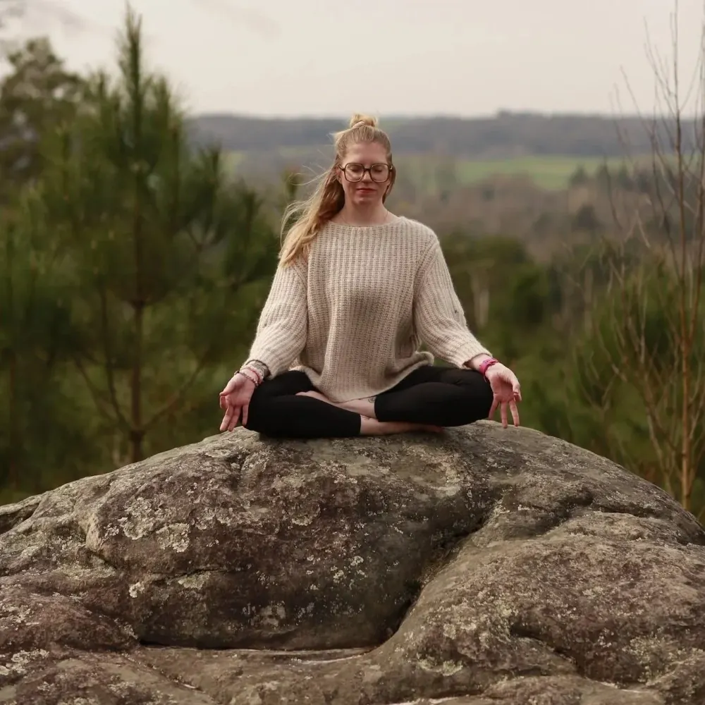 Professeure de yoga à Salins (77) : Delphine en méditation assise sur un rocher, dans un paysage naturel