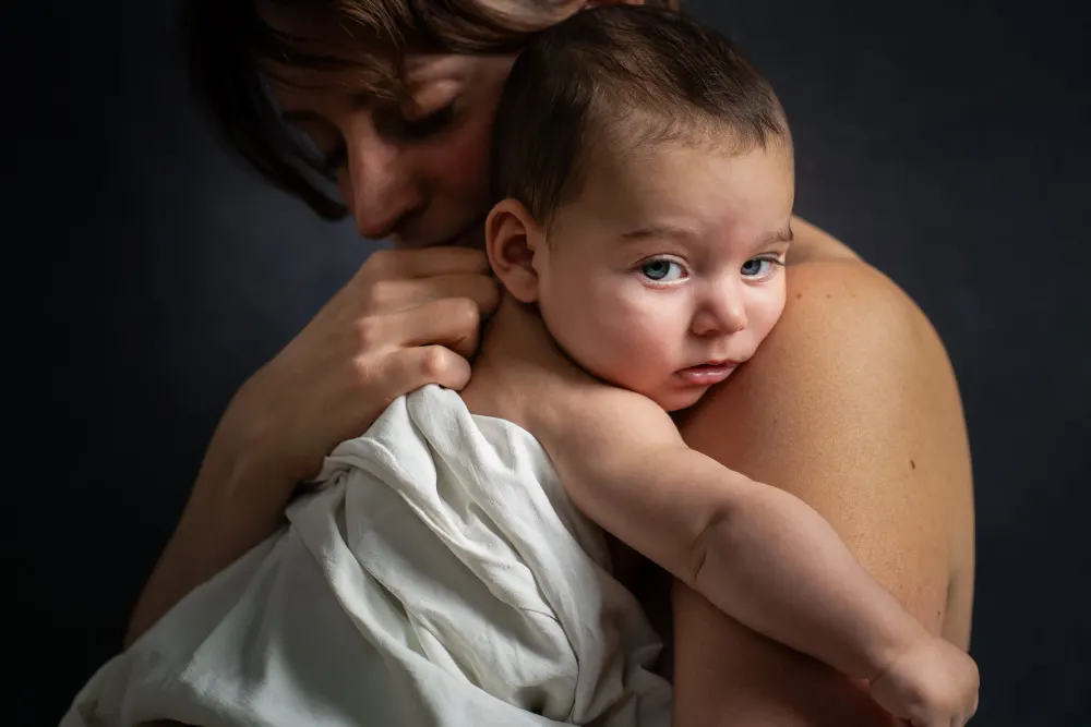 Photographie de famille à Salins : un parent serre tendrement un jeune enfant aux yeux bleus
