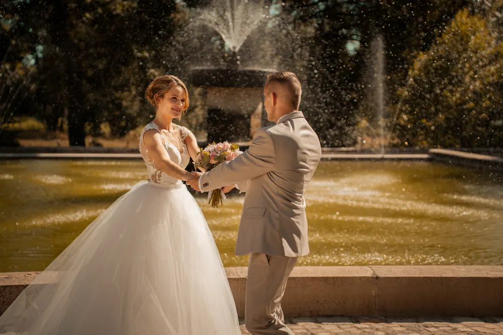 Séance photo de couple le jour du mariage : les mariés main dans la main devant une fontaine