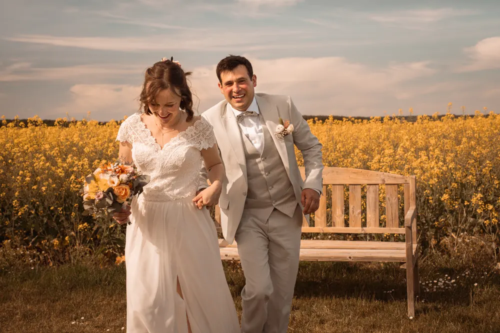 Shooting photo couple de mariés près de Salins (77) : les mariés courent main dans la main dans un champ de colza