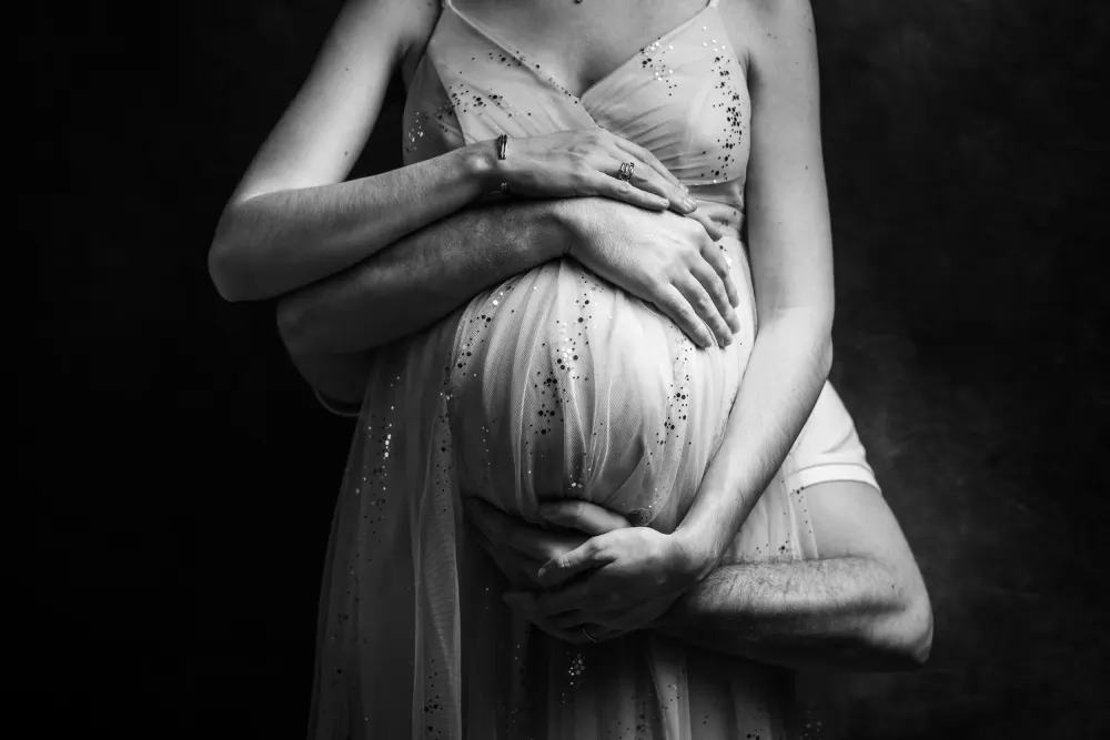 Shooting photo grossesse en Seine-et-Marne : femme enceinte en robe élégante soutenue par son conjoint, photographie en noir et blanc